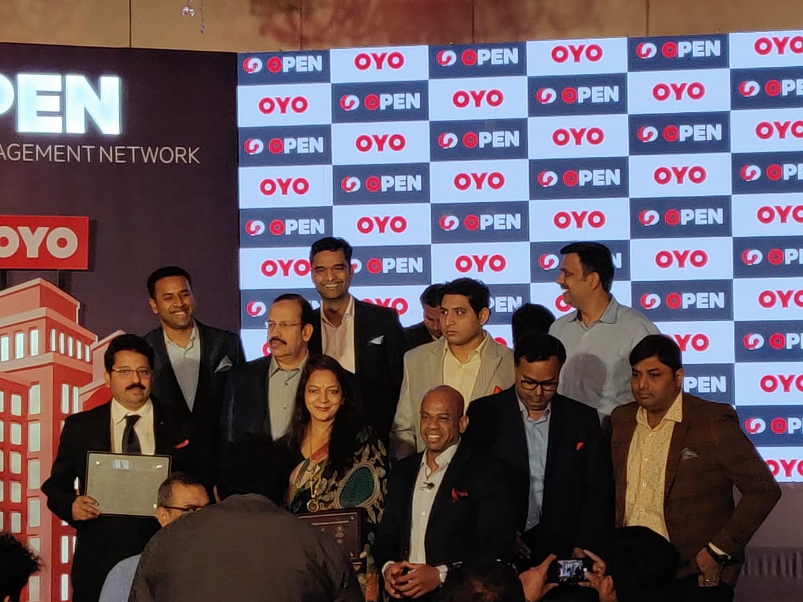 Ex.13 — OYO OPEN launch, closing group photo against the step-and-repeat